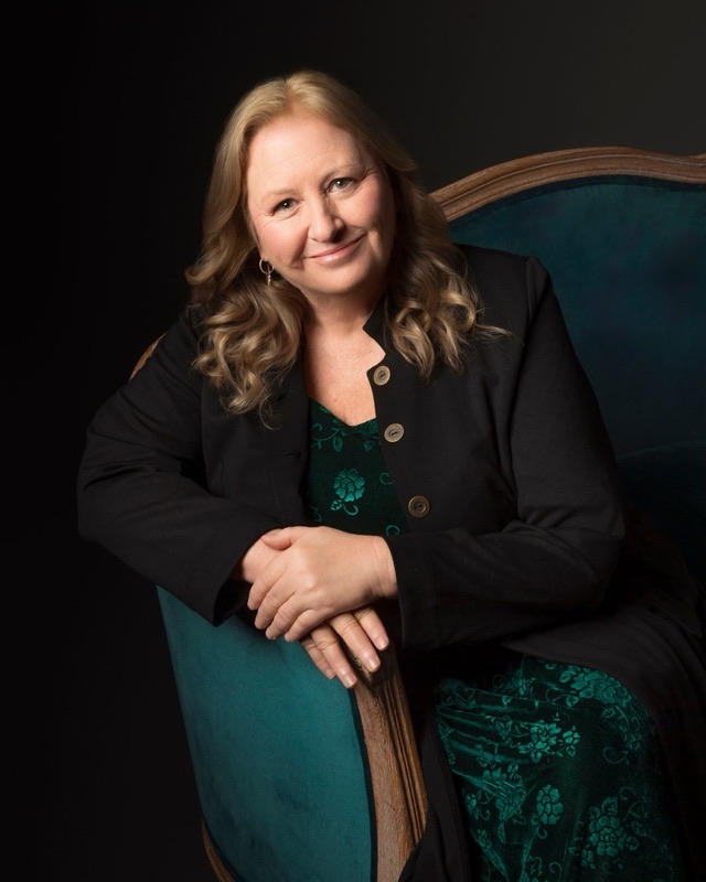 Donna Foster, founder of Mortal Me, seated in a velvet armchair and smiling